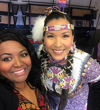 Two staff members posing together as one is dressed in Native American attire